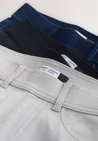 Trois leggings en jersey pleine longueur, pliés, en gris clair, noir et bleu foncé, montrant les ceintures et les étiquettes.