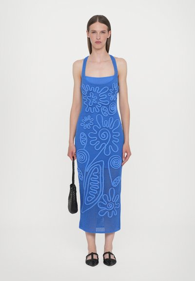 Vestido de ganchillo azul con recortes que presenta patrones florales y abstractos. Corte recto, diseño de cuello halter, combinado con un bolso negro y zapatos.