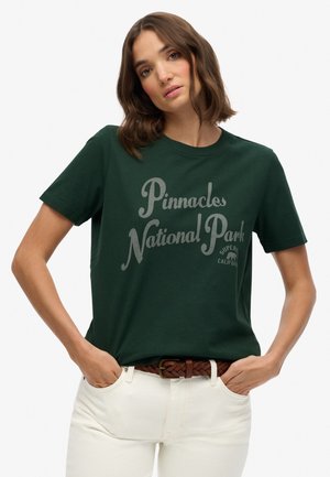 T-shirt en coton vert foncé avec un imprimé graphique gris portant l'inscription "Parc national des Pinnacles". Col rond classique et manches courtes.