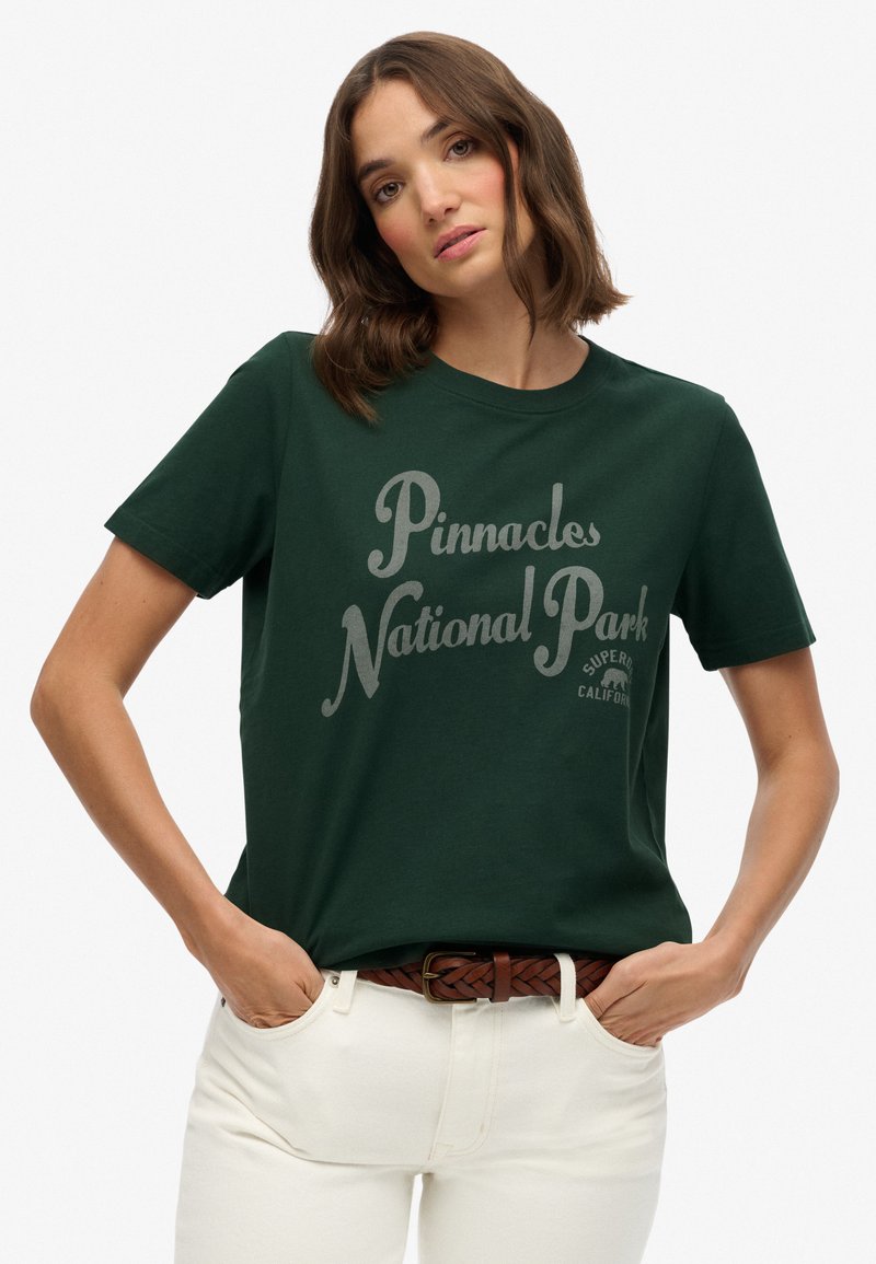Mørkegrøn bomulds T-shirt med et gråt grafiktryk, der står "Pinnacles National Park." Klassisk rund hals og korte ærmer.