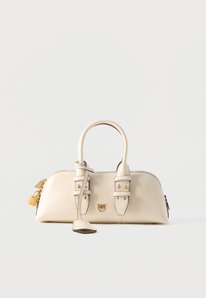 Sac à main en cuir crème avec deux poignées, garnitures dorées, détails de boucles et un petit cadenas attaché sur fond blanc.