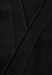 Svart stickad cardigan med V-ringning och ribbat mönster vid kanterna. Mjuk, lätt tyg mostrar fina detaljer.