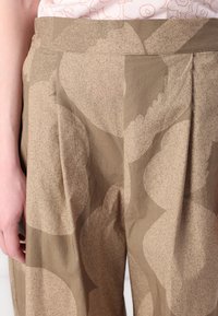Beige patterned trousers with large abstract shapes. Made of a lightweight fabric featuring subtle texture and pleated design.