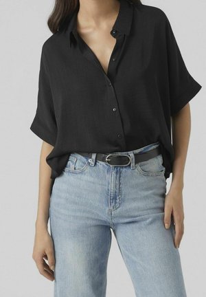 Sort kortermet skjorte med knap i letvægtsstof, parret med højtaljede lyseblå jeans og et sort bælte med en sølvspænde.