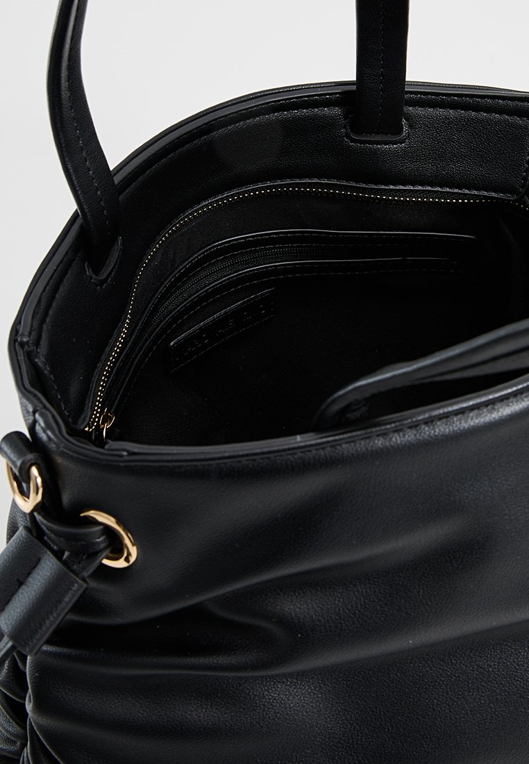Interior de bolso de cuero negro con bolsillos con cremallera y textura suave. Presenta acentos de hardware dorado y una abertura superior redondeada.