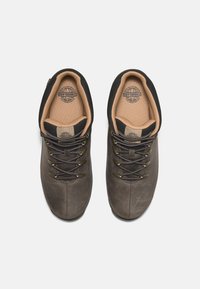 Ciemnobrązowe skórzane buty trekkingowe z czarnymi akcentami, okrągłym noskiem, srebrnymi detalami, sznurowadłami i wyściełanymi beżowymi wkładkami. Gładka tekstura.