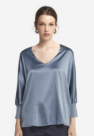 Blaue Satinbluse mit V-Ausschnitt, dreiviertel Ärmeln und lockerer Passform, die eine glatte Textur und ein minimalistisches Design aufweist.