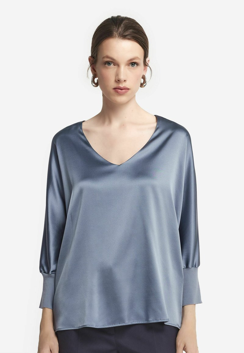 Blaue Satinbluse mit V-Ausschnitt, dreiviertel Ärmeln und lockerer Passform, die eine glatte Textur und ein minimalistisches Design aufweist.