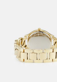 Gouden polshorloge met een brede, gekoppelde metalen armband en een ronde kast. Glad, reflecterend oppervlakte met een eenvoudig ontwerp.