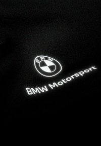 Zwarte stof met een wit BMW-logo en de tekst "BMW Motorsport." Soepele textuur met een minimalistisch ontwerp en duidelijke branding.