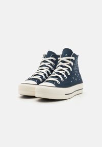 Zapatillas altas de lienzo marino con patrón de estrellas blancas, que cuentan con cordones blancos y suela de goma con superficie texturizada y detalle de rayas negras.