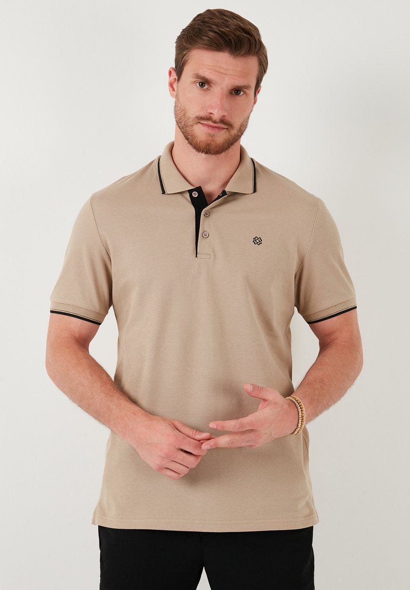 Beige polo ing fekete gallérral és díszítéssel, rövid ujjakkal, texturált anyagból, háromgombos záródással és logóval a bal mellrészen.