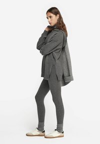 Maglione grigio a maglia con collo alto, spacco laterale e leggings grigi abbinati. Indossato con sneakers bianche e beige. Design semplice e testurizzato.
