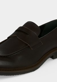 Mocassin en cuir marron foncé à surface texturée, petit talon, bout arrondi et détail de bride sur le dessus.
