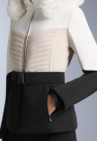 Padded jakna s krznim ovratnikom, u boji krem, bež i crnoj. Ima romboidni uzorak i pojas u struku sa bočnim džepovima.