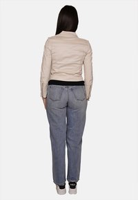 Giacca di pelle beige, top nero e jeans dritti azzurri chiari. Le caratteristiche includono tasche posteriori e sneakers bianche con accenti neri.