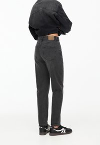 Black denim high-waisted jeans with a straight leg cut, featuring two back pockets and a brown leather patch on the waistband.