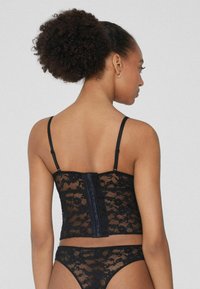 Schwarzer Spitzen-Bodysuit mit verstellbaren Trägern, der ein florales Muster aufweist und einen Haken- und Ösenverschluss auf der Rückseite hat. Weicher Stoff mit taillierter Passform.