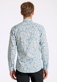 Blommig skjorta i ljusblått tyg med gula och blå blommönster. Långa ärmar med knappmanchetter och en rundad nederkant.