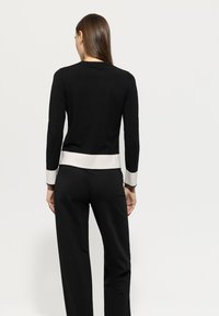 Schwarzer gestrickter Pullover mit langen Ärmeln und einem weißen Saum sowie Bündchen. Einfaches Design, taillierte Form und strukturierter Stoff.