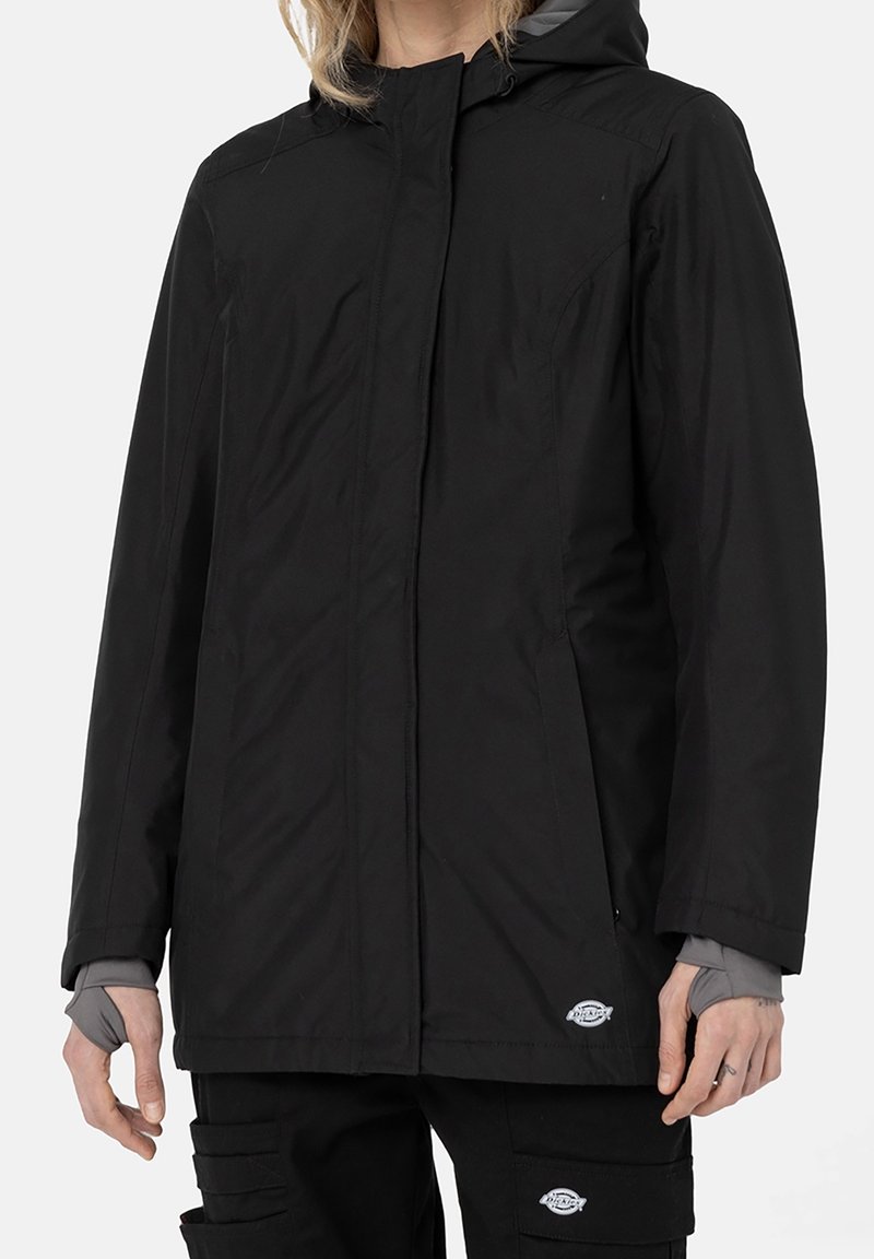 Svart vattentät jacka med huva, dragkedjeöppning, sidofickor och en slät yta. Har en logotyp på den nedre fållen och elastiska ärmslut.