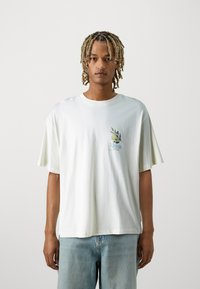 Camiseta de algodón blanca con mangas cortas, que presenta una impresión gráfica colorida de limones y hojas en el lado izquierdo del pecho. Corte relajado.