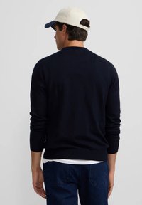 Suéter azul marino hecho de tela suave, con mangas largas y un dobladillo acanalado. Combinado con jeans de mezclilla y una gorra de color claro.