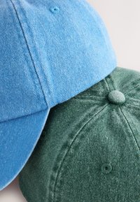 Deux casquettes de baseball structurées empilées ; l'une est bleu clair et l'autre vert foncé. Les deux présentent un tissu texturé et des boutons sur le dessus.