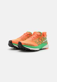 Helle orange und grüne Trailrunningschuhe mit strukturierten Mesh-Obermaterialien, schwarzen Gummi-Außensohlen und gewellten Mustern auf der Zwischensohle.