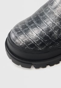 Μαύρο μποτάκι πλατφόρμα με υφή μεταλλικού ασημί κροκοδειλόδερμα, με παχύ μαύρο πάτο και στρογγυλεμένο σχέδιο μύτης.