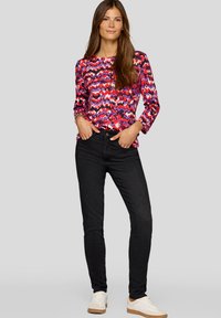 Long-sleeve shirt with a multicolored zigzag pattern in pink, red, and purple, paired with black jeans and white sneakers.