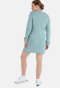 Robe tricotée bleu clair avec des manches longues, texture côtelée, fentes sur les côtés et une petite étiquette logo ; associée à des baskets montantes blanches.