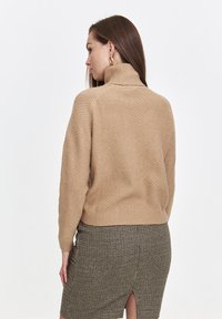 Beżowy sweter z golfem, dziany, z teksturowanym wzorem, prążkowanymi mankietami i skróconym dołem, w zestawieniu z ołówkową spódnicą w wzory.