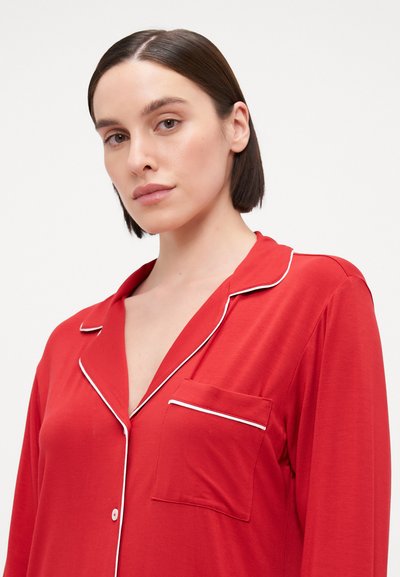 Camisa de pijama vermelha com detalhes em branco, frente com botões, gola de lapela e um bolso no lado esquerdo. Tecido suave com uma textura lisa.