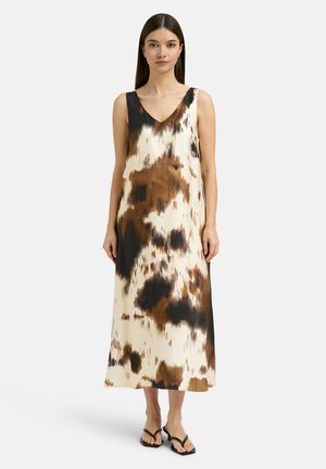 Woman wearing a brown, black, and cream sleeveless midi dress with abstract print and black flat sandals standing against a plain background.