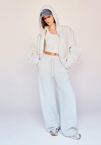 Svetlošedá oversize mikina a zodpovedajúce tepláky, ktoré sa vyznačujú príjemnou textúrou a elastickým pásom. Doplnkové s denimbovou šiltovkou a teniskami.
