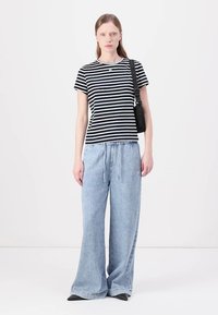 Camiseta a rayas blanca y negra combinada con pantalones de chándal de pierna ancha en azul claro. Incluye un bolso negro con una correa de marca.