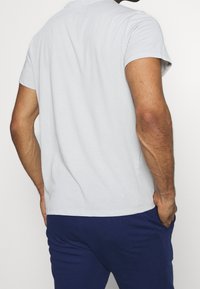 Camiseta de manga corta color gris claro, con cuello redondo, de tejido de algodón y ajuste regular. La vista trasera muestra una textura suave y un diseño sencillo.