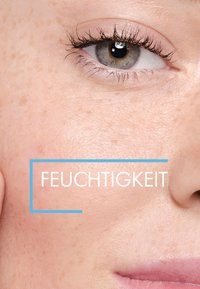 Close-up of skin showing light complexion with freckles, smooth texture, and an eye with gray-blue iris. Text overlay reads "FEUCHTIGKEIT."