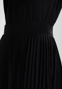 Vestido negro con pliegues y una cinturilla ancha y suave. Hecho de una tela suave, presenta rayas verticales en los pliegues y una silueta fluida.