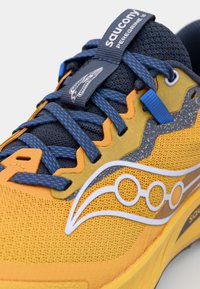 Felgeel hardloopschoen met blauwe accenten, geweven bovenkant met textuur, gelaagd ontwerp, prominente Saucony-logo en gemusterde veters.