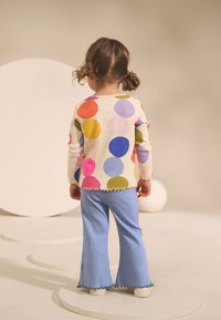 Majica dugih rukava s šarenim točkicama u rozoj, plavoj, žutoj i zelenoj boji. Plave rebraste široke hlače. Teksturirani materijal. Zaobljeni rub.