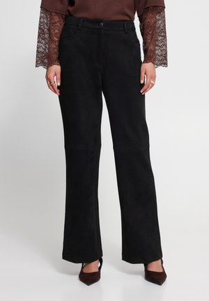 Pantalon noir taille haute à jambes larges porté par une personne avec des manches longues en dentelle marron et des talons marron à bout pointu.