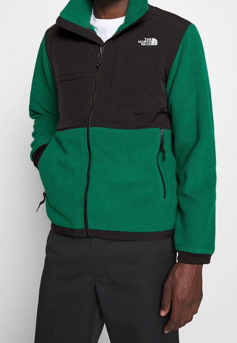 Fleece bunda se zeleným tělem a černými rameny, s předním zipem, dvěma bočními kapsami a kapsou na prsou. Logo na levé straně.