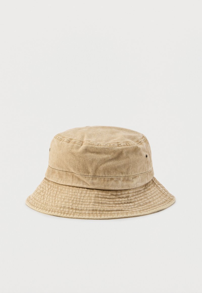 Chapeau bob beige en coton avec bord cousu et petits œillets de ventilation sur un fond blanc uni.
