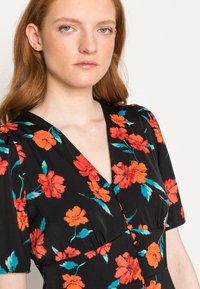 Vestido preto com padrão floral, apresentando flores vermelhas e turquesas, mangas curtas em puff, decote em V e botões na parte da frente para fecho.