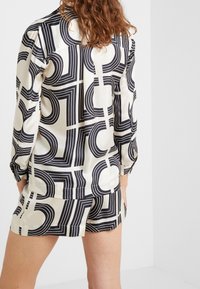 Chemise en soie à motif géométrique noir et blanc avec des manches longues, présentant des lignes courbes et droites, associée à un short assorti.