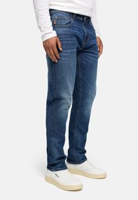 Blå denimjeans med rett passform, preget av falmet finish, fem lommer og knappeåpning, brukt med hvite joggesko.