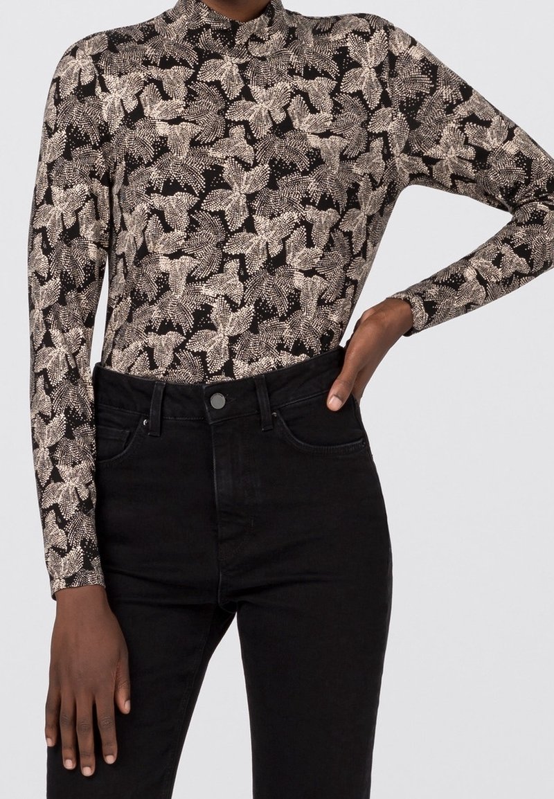 Svart långärmad topp med hög hals, texturerad tyg med ett krämfärgat bladmönster, tillsammans med högmidjade svarta jeans.