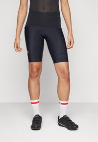 Sorte sykkelshorts med tettsittende passform, glatt stoff og en rød logo. Kombinert med hvite sokker med røde og grå striper og svarte sykkelsko.